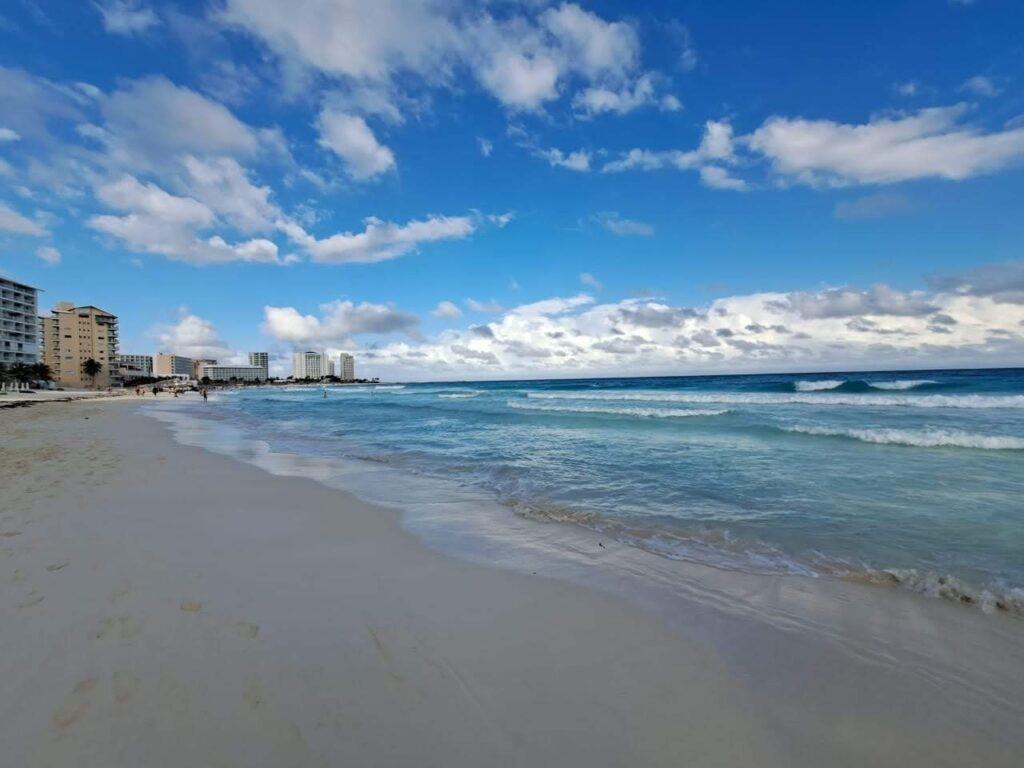 Wide sand beach and surf at Playa Tortugas in the Cancun Hotel Zone with towers in the distance