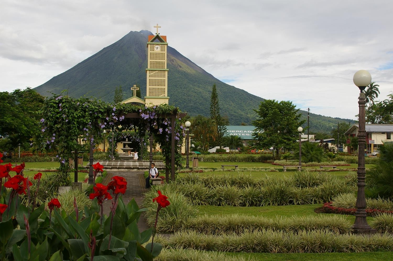 Arenal Volcano rising behind a church tower and flower gardens in La Fortuna, Costa Rica