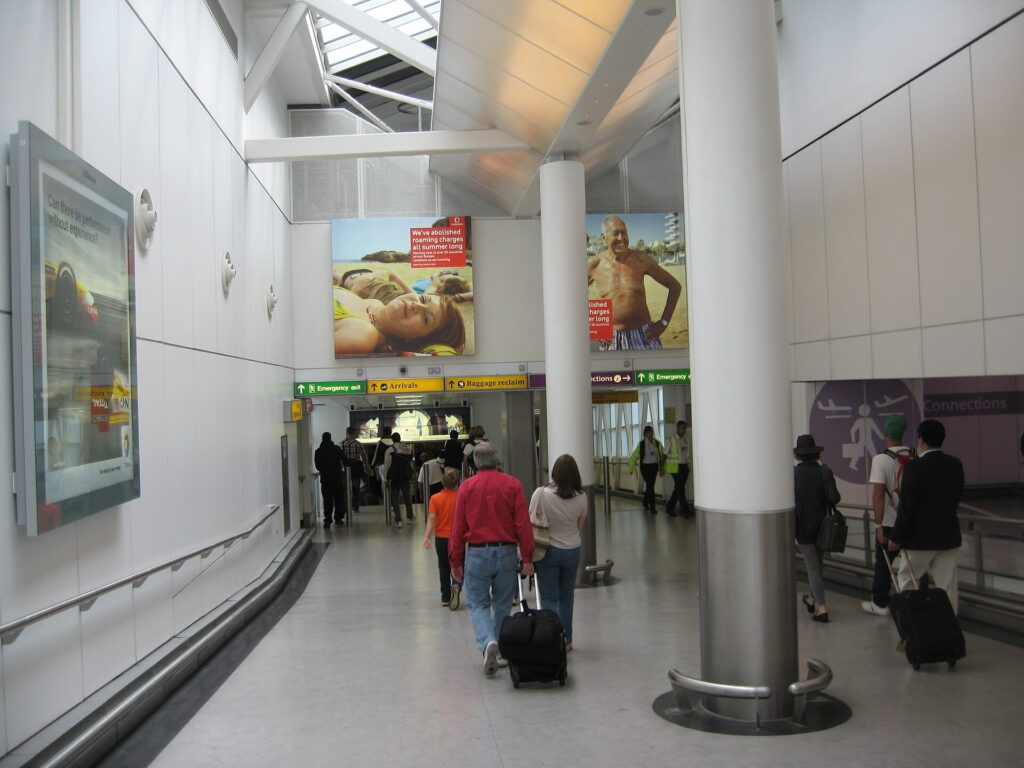 Travelers with wheeled bags walking the arrivals corridor at London Heathrow Airport
