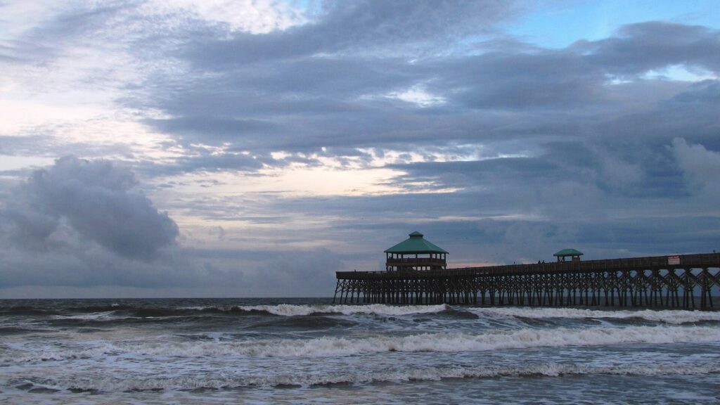 Folly Beach pier reaching over rough surf under a cloudy sky
