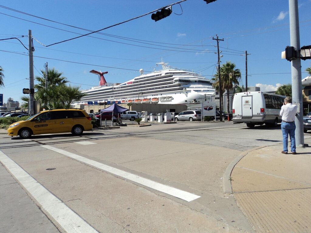 Carnival Conquest cruise ship docked at the Port of Galveston beyond a street corner with cars and a taxi