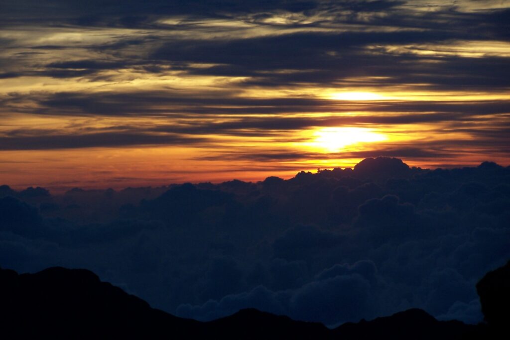 Sun setting through bands of cloud above dark ridgelines at Haleakala on Maui