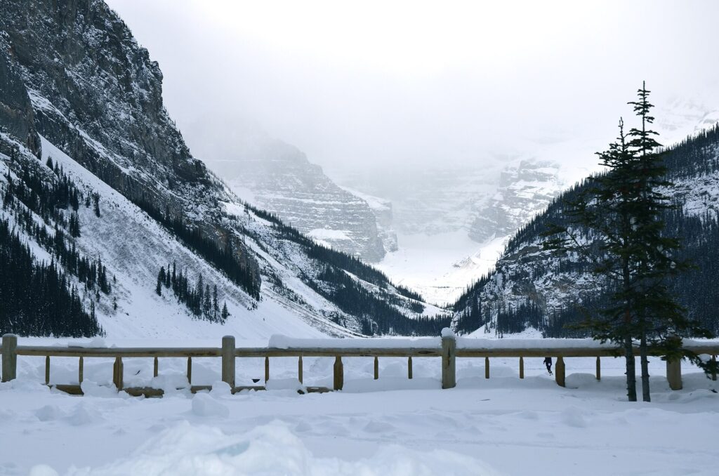 Snow-covered shore of Lake Louise with a fence and mountains in winter