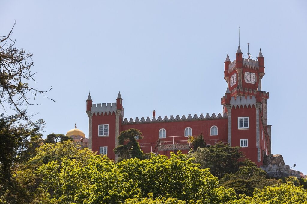 Red tower and battlements of Pena Palace rising above trees in Sintra, Portugal