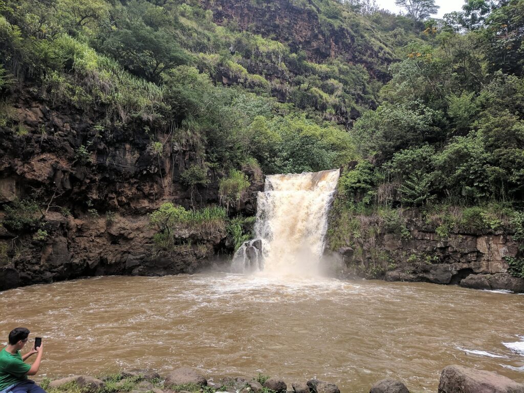 Waterfall dropping into a muddy brown pool surrounded by green cliffs in Waimea Valley
