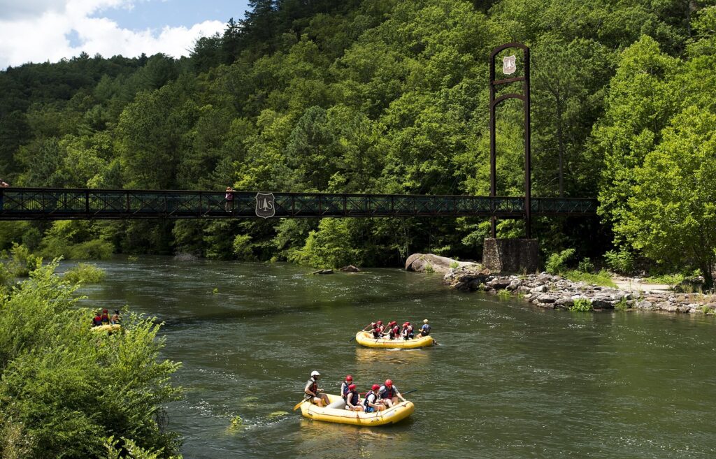 Two rafts drifting down a calm stretch of the Ocoee River past a hanging footbridge in Tennessee