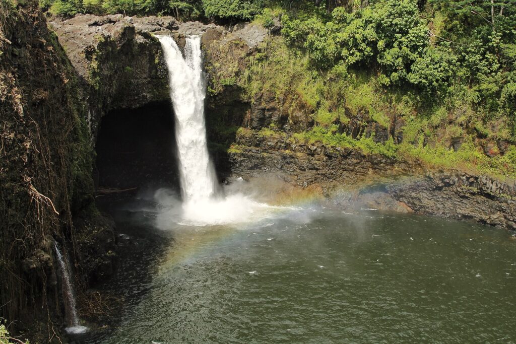 Rainbow Falls dropping over a rock ledge into a green gorge, with a faint rainbow in the mist, in Hilo on the Big Island