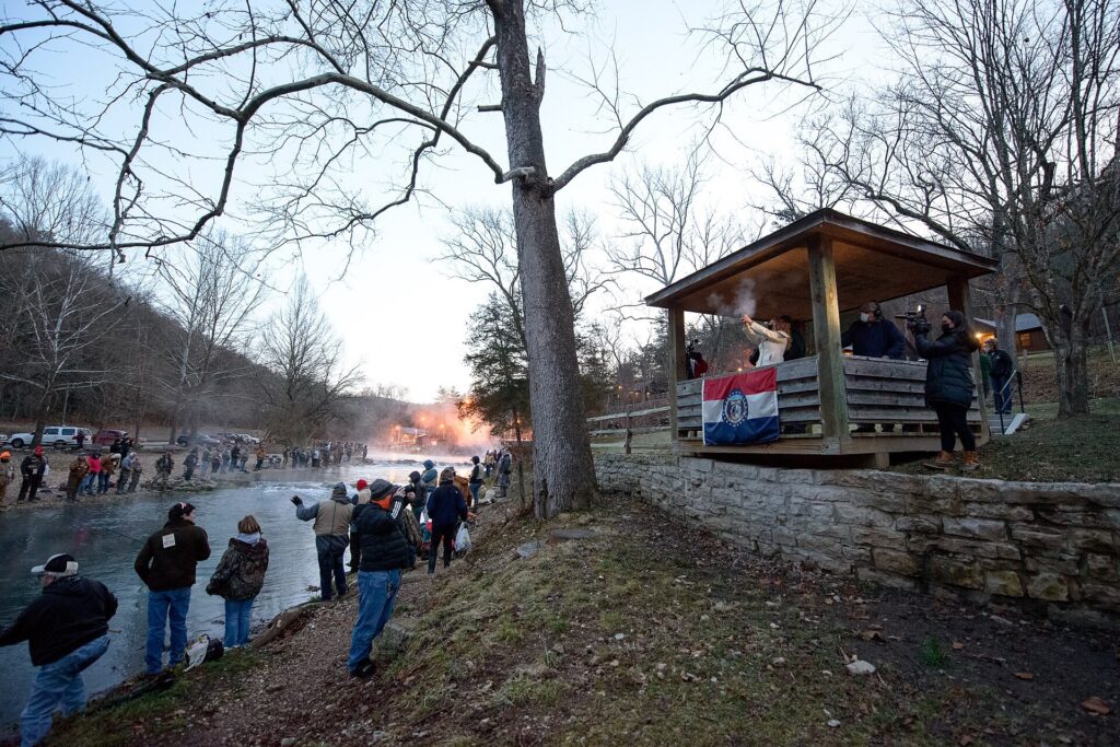 Opening-day anglers along the creek bank beside a wooden picnic shelter at Roaring River State Park, Missouri