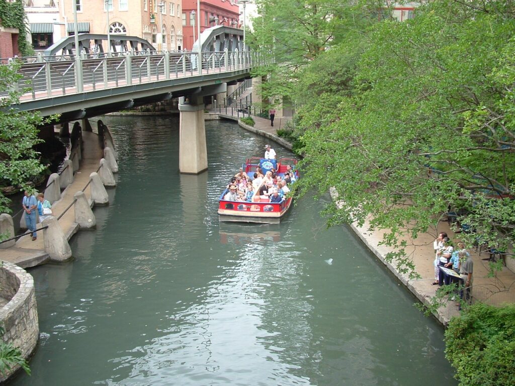 Tour boat on the San Antonio River Walk beneath a footbridge and trees