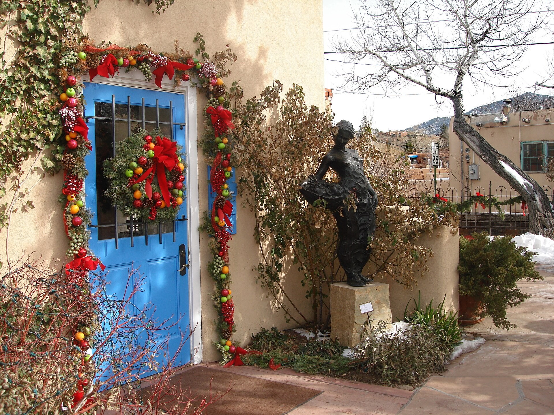 A blue door framed by a red wreath and a bronze statue in an adobe courtyard on Canyon Road in Santa Fe, New Mexico