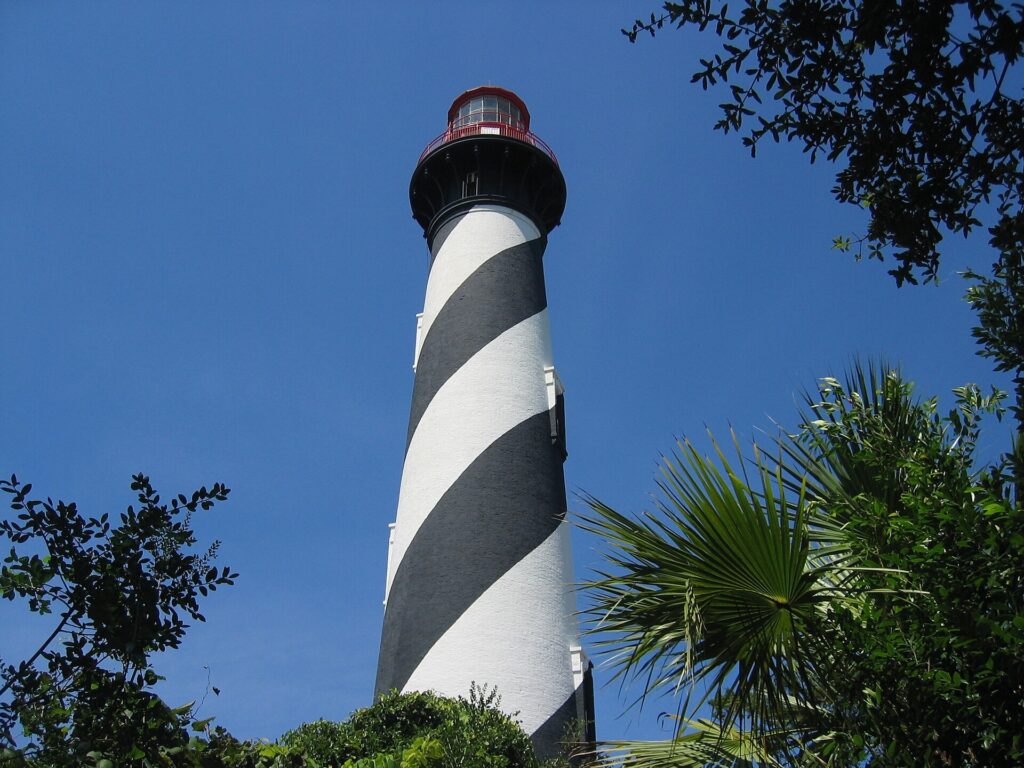 The black-and-white striped St. Augustine Lighthouse tower rising above palm fronds