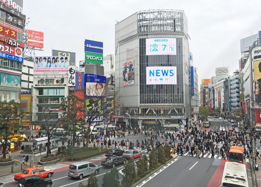 Pedestrians crossing the Shibuya scramble crossing beside shop signs and buses in Tokyo
