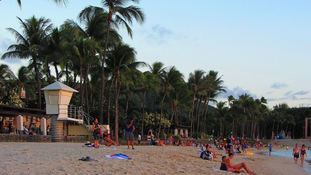 Beachgoers on the sand under palm trees beside a lifeguard tower in Waikiki