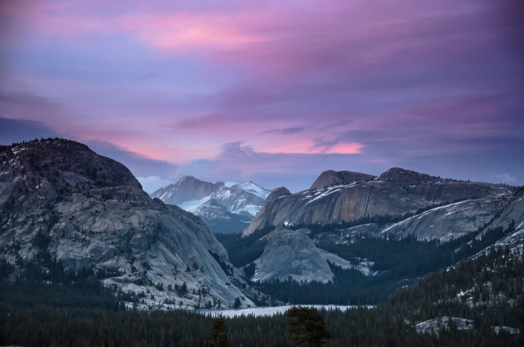 Granite domes and a strip of Tenaya Lake under a pink sunset sky in Yosemite’s high country
